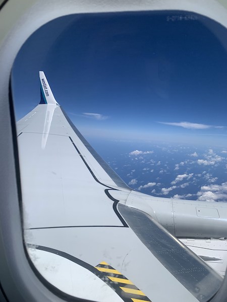 View from the window seat of the airplane of the WestJet airplane wing and Pacific Ocean.